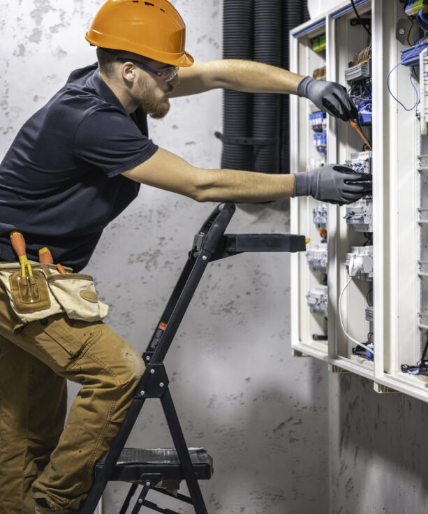 A male electrician works in a switchboard with an electrical connecting cable.